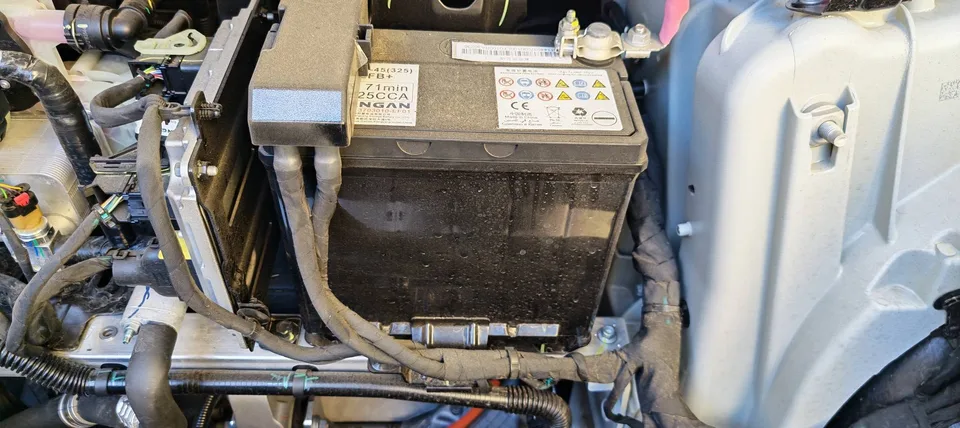 Close-up of the installed 12V battery with its label partly obscured by the positive-terminal assembly