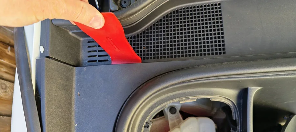 Plastic trim tool inserted at a rear corner of the front boot liner